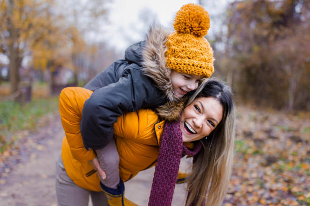 Cheerful mother piggybacking her small boy in autumn day in nature. Cheerful single mother piggybacking her small son in nature. piggyback photos stock pictures, royalty-free photos & images