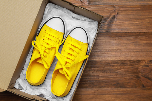 Pair of stylish sport shoes in cardboard box on wooden background, top view. Space for text