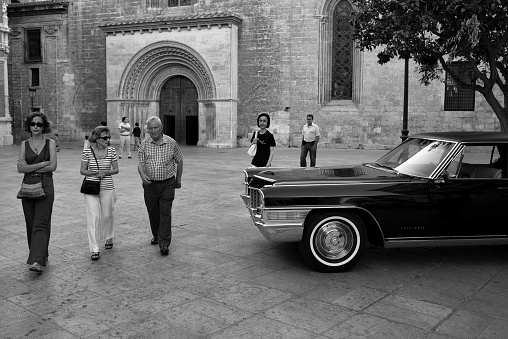 valencia spain july 16 - 2016 unknown people walk in a square in valencia city and they walk past a black car and next to a church next to the plaza de la virgen.