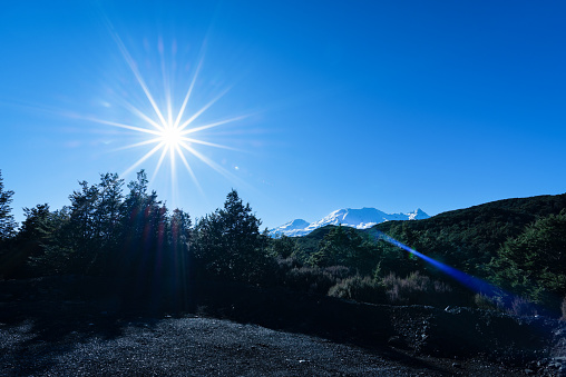 Bright starburst sun shining over snow-capped Mt Ruapehu, North Island, New Zealand