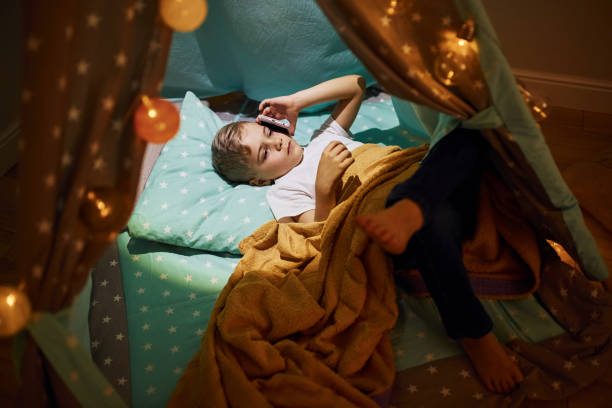 istock Using phone. Young boy in casual clothes lying down in tent at evening time 1328458439