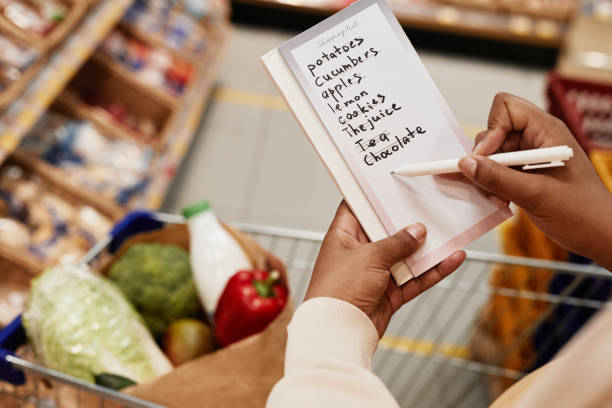 Woman Crossing Items of Shopping List Close up of unrecognizable African-American woman holding shopping list while buying food in supermarket, copy space shopping list stock pictures, royalty-free photos & images