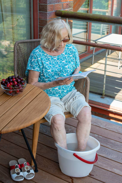 mujer mayor relajante libro de lectura y pies empapados en el agua fría. cómo mantenerse fresco en climas calurosos. - enfriamiento fotografías e imágenes de stock