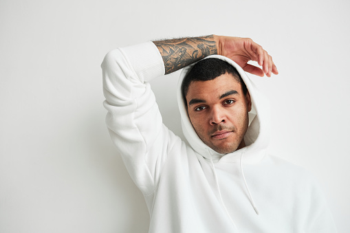 Minimal portrait of tattooed young man wearing white hoodie and looking at camera, copy space