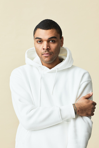 Minimal waist up portrait of handsome mixed-race man wearing white hoodie and looking at camera while posing against yellow background