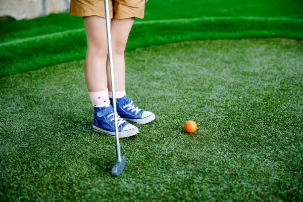 Cute preschool girl playing mini golf with family. Happy toddler child having fun with outdoor activity. Summer sport for children and adults, outdoors. Family vacations or resort