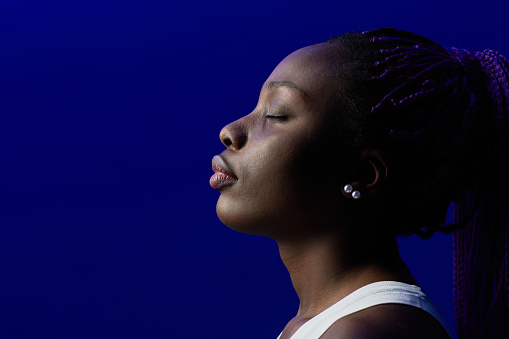 Minimal side view portrait of young African-American woman with eyes closed against purple background in studio, copy space