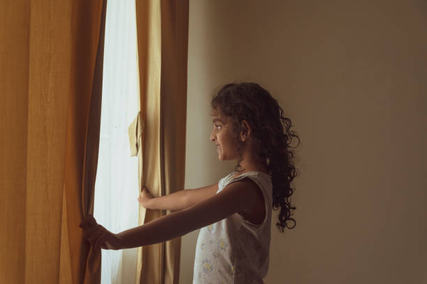 istock little girl looking through a house window 1328463748