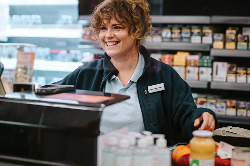 Female grocery store manager working at checkout counter. Woman cashier working at supermarket checkout.