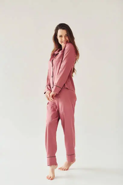 Photo of Cheerful young woman in pajamas standing indoors against white background in the studio