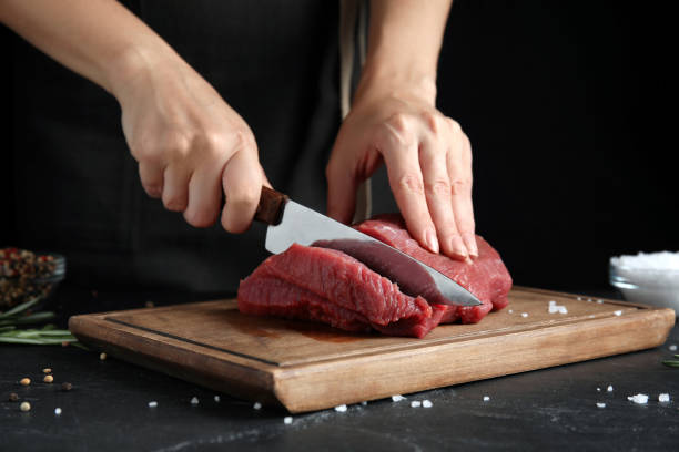 istock Woman cutting fresh raw meat at black table, closeup 1328469287