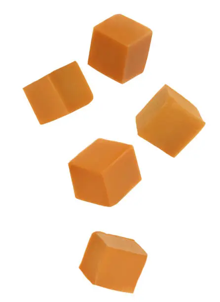 Photo of Delicious caramel cubes flying on white background