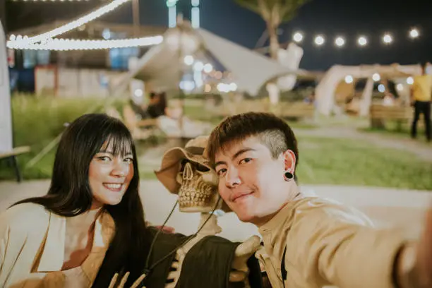 Photo of Selfie,Young Thai couple look at smart phone for lovely selfie during dating in Haloween concept exhibition at night camping cafe - stock photo