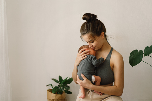 Mother holds and hugs her newborn baby son at home. Happy infant and mom. Mother's day concept