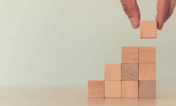 istock Business growth and management concept. Stack wood cubes on light background. Hand arranging wood cube stacking as stair step shape, mock up for create symbol or logo. Copy space. 1328476678