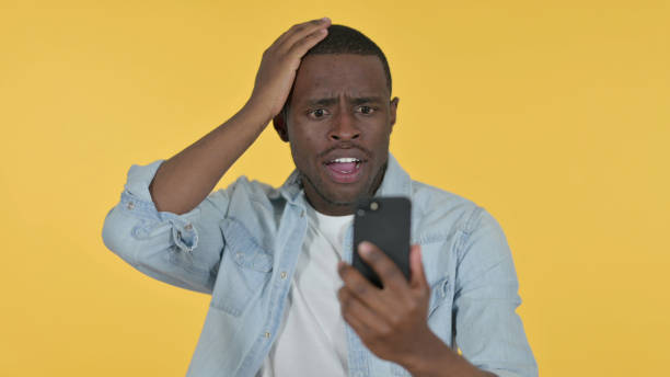 istock Young African Man Loss on Smartphone, Yellow Background 1328477446
