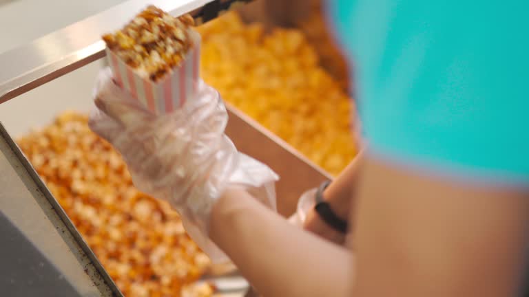 fast-food worker scooping filling stuffing popcorn into paper bucket at Concession stand in entertainment building cinema movie theater cinema