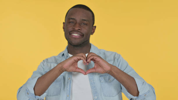 istock Young African Man Heart Sign by Hand, Yellow Background 1328477749