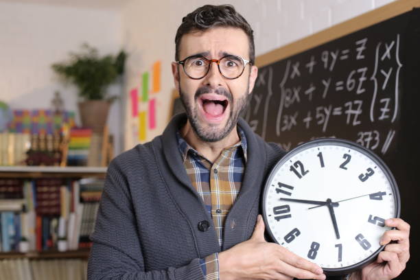 lehrer hält große uhr im klassenzimmer - hispanic male stock-fotos und bilder