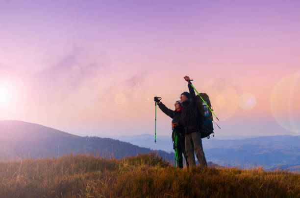 Hiker couple with backpacks meets sunset on the mountain top. Active lifestyle and wanderlust concept stock photo