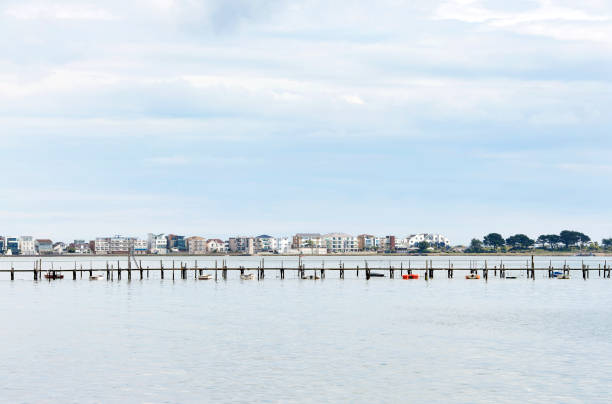 A distinctive blue sky sits over the scenery, properties and houses that skirt the Sandbanks Road around the natural water of Poole Harbour where a long old jetty for small boats contrasts with the opulence of the homes in this view around Poole Harbour view, Dorset, England