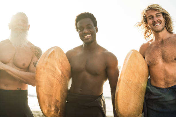 istock Multi generational surfer friends having fun on the beach after surf session - Soft focus on right man 1328482142