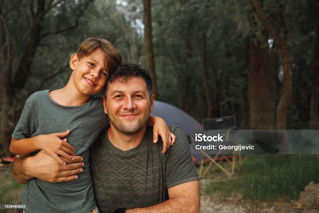 Family camping A smiling father and son hug and pose for the photo in front of a tent while camping in nature. Father Stock Photo
