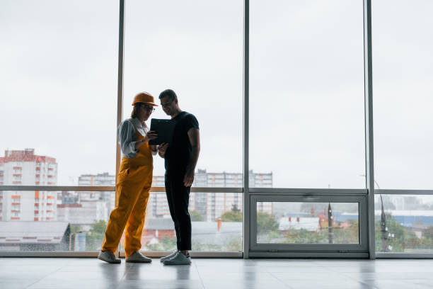 istock Female worker or engineer in yellow uniform and hard hat standing indoors with man 1328488034