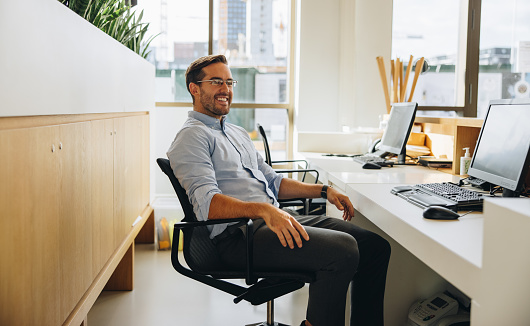 Executive taking break from work. Entrepreneur sitting relaxed at desk in office looking away and smiling.