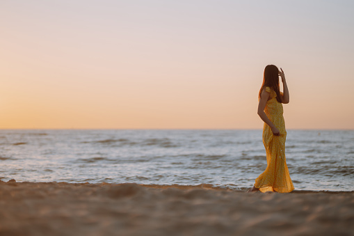 Beautiful woman on the beach at sunset. ​She is enjoying serene ocean nature during travel holidays vacation outdoors. Summer time.