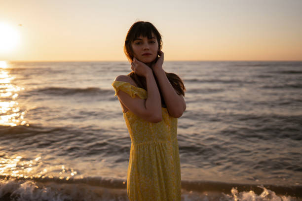 Beautiful woman on the beach at sunset. ​She is enjoying serene ocean nature during travel holidays vacation outdoors. Summer time.