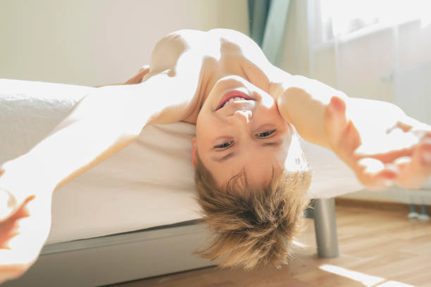 istock Cute boy laughs lying on the bed upside down 1328493217