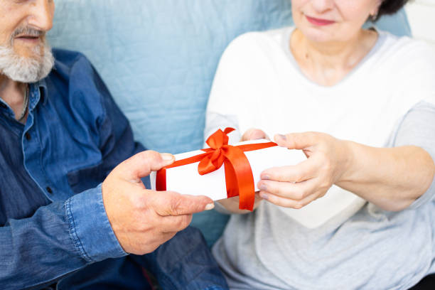 close up of gift box with red bow in hands of senior couple. mature man making surprise for wife, expressing his love and feelings. celebration and congratulation of birthday,anniversary or christmas - men latin american and hispanic ethnicity southern european descent mature adult imagens e fotografias de stock