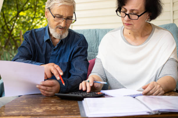 hombre y mujer de edad avanzada con anteojos examinando documentos y facturas, usando la calculadora teniendo en cuenta la cantidad de atrasos en el alquiler, revisando las finanzas, administrando los gastos domésticos, sentado en la terraza de la casa - armenian ethnicity fotografías e imágenes de stock