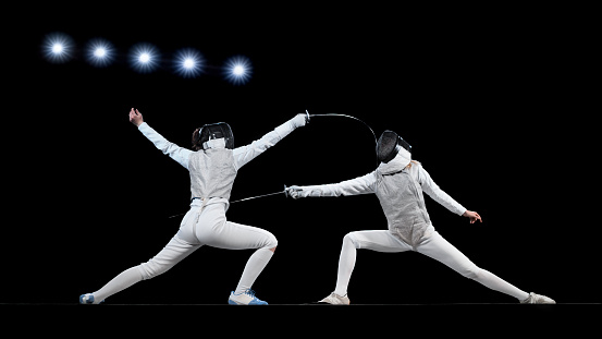 Female fencing athletes fighting against black background ..