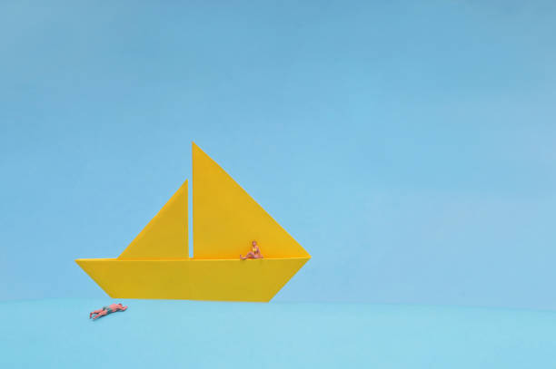 Conceptual Yellow Paper boat and Miniature People On Blue Background stock photo
