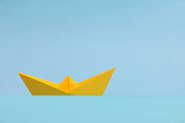 istock Conceptual Yellow Paper boat On Blue Background 1328497666