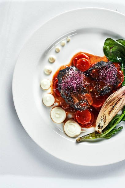 istock Braised beef cheeks with vegetables on a white plate Cooking beef cheeks in demigas sauce with grilled spinach leaves and carrots light background top view 1328497834