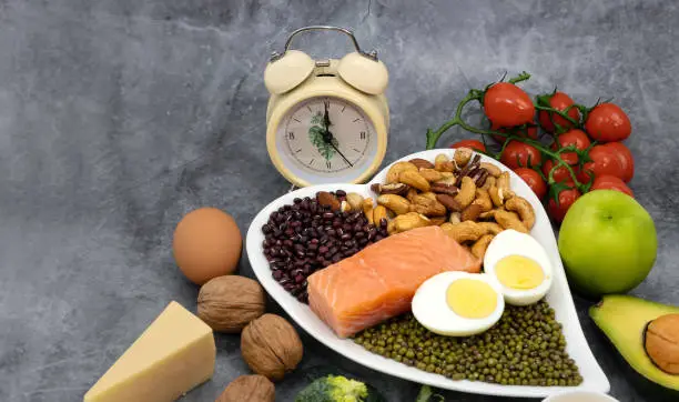 Photo of Healthy food  in plate  and alarm clock which a healthy of Keto diet food ingredients on  the  table.Ketogenic mean Low carb and High fat.