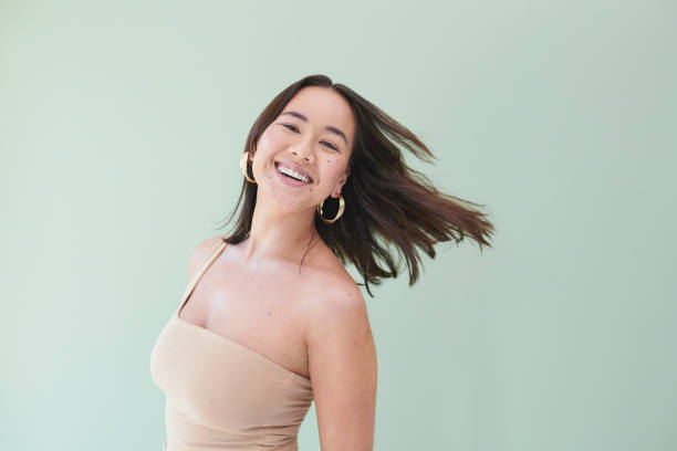 Cropped studio portrait of a young beautiful woman tossing her hair against a green background stock photo