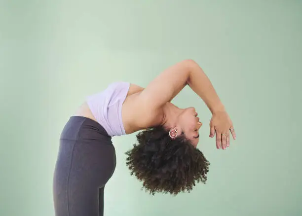 Photo of Studio shot of a young woman bending over backwards against a green background