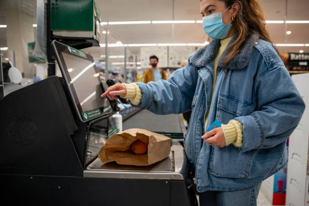 Weighing Fresh Items At The Till Inside view of a young woman selecting her products from the till to make sure she gets the correct price she is using a touchscreen till and is also wearing a protective facemask whilst inside the supermarket to protect yourself and others during the pandemic. self checkout photos stock pictures, royalty-free photos & images