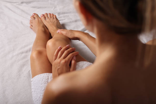 Woman applying healthy body cram on legs after bathing in bed stock photo