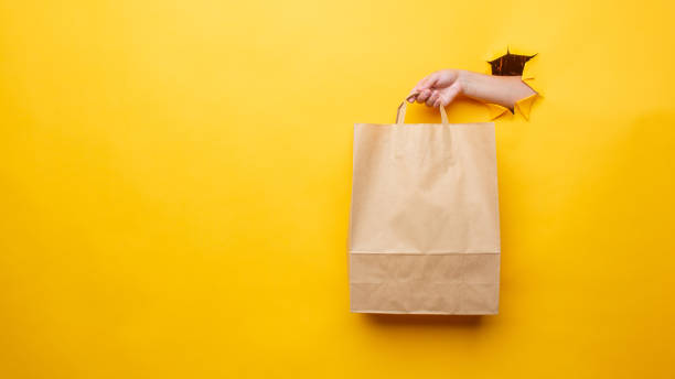 istock A woman's hand with an paper bag on a yellow background 1328510414
