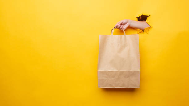 женская рука с бумажным пакетом на желтом фоне - paper bag bag paper brown стоковые фото и изображения