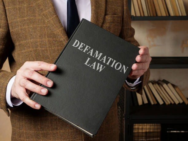 istock Lawyer in suit holds Defamation law book. 1328513644