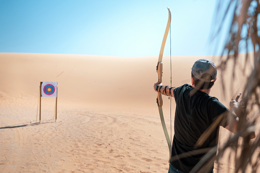 Man practicing archery and using bow and arrow to hit the target in the desert. Hobby and leisure with vacation concept