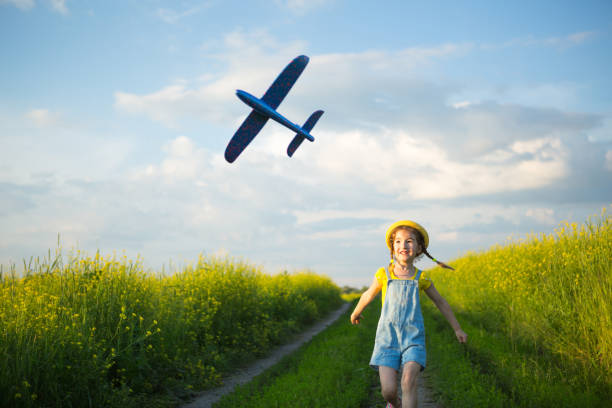 une fille au chapeau jaune panama lance un avion-mouche dans le champ. heure d’été, enfance, rêves et insouciance. visite en avion d’une agence de voyages lors d’un voyage, d’une aventure et de vacances. village, noyau de chalet - fighter plane photos et images de collection