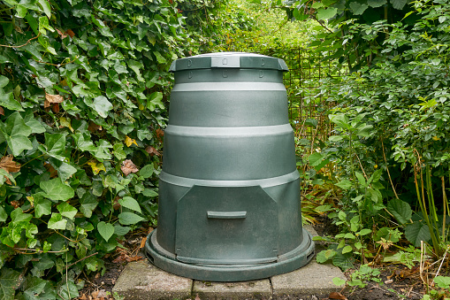 Round green compost bin made of recycled plastic in a garden. Recycling and eco friendly concept.