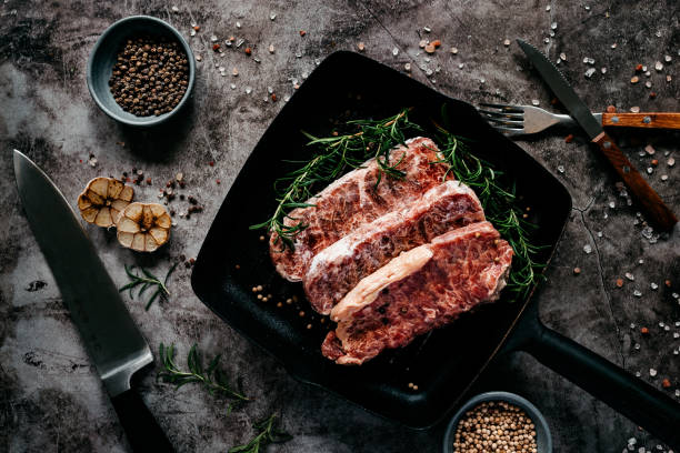 Close up raw wagyu beef striploin steak with pepper on dark pan stock photo